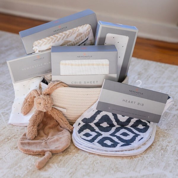"Cherish Bundle: Welcome Baby gift set featuring newborn essentials in gender neutral colors, perfect for new arrivals. Cozy and adorable setting."
