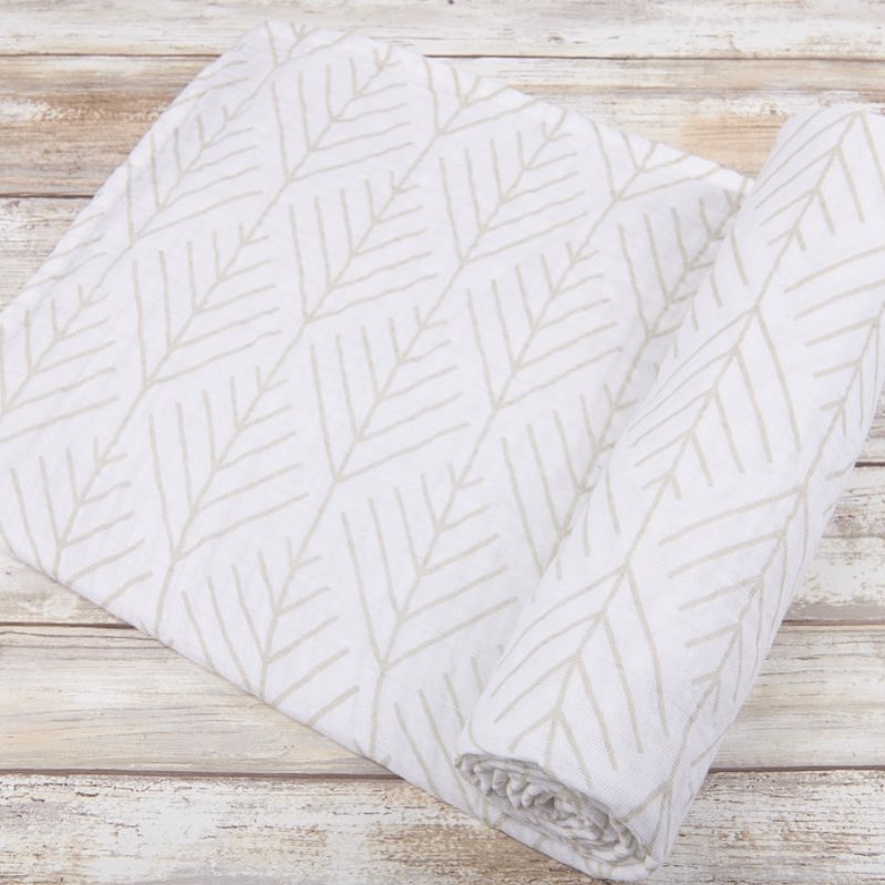 White swaddle cloth with a light branch pattern, folded and partly rolled on a wood surface.