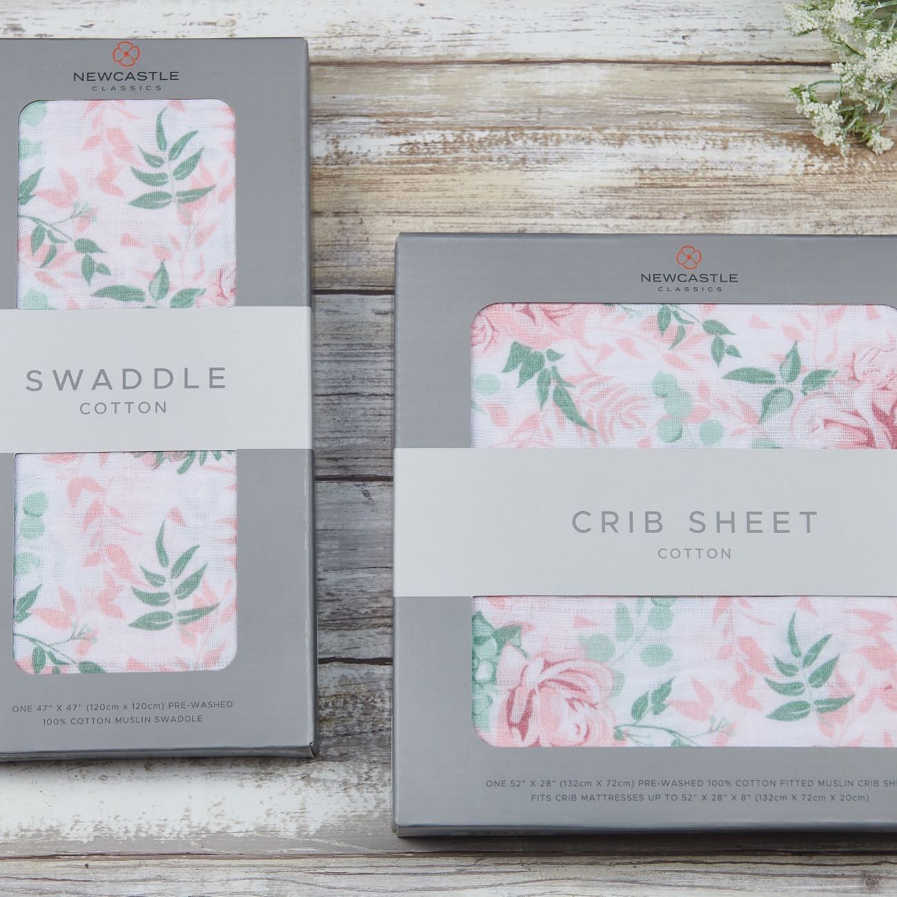 Packaged pink floral crib sheet and matching swaddle on a rustic wood background.