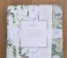 Folded baby blanket set with three visible prints and a paper wrap on a wood floor.
